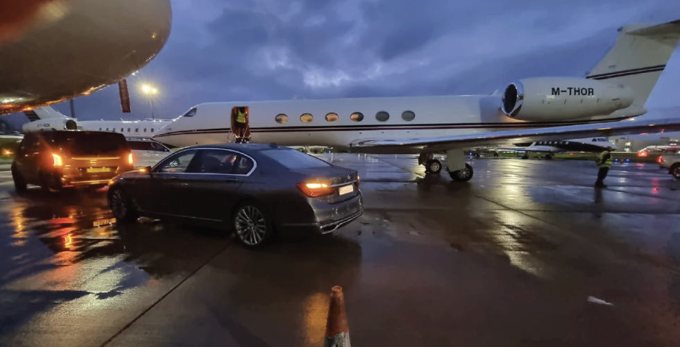 Executive car waiting on the apron beside a private jet at dusk